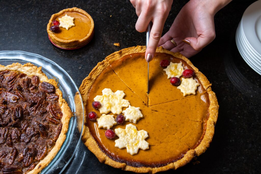 A pumpkin pie garnished with cherries and white icing decorations being shown as someone is slicing it