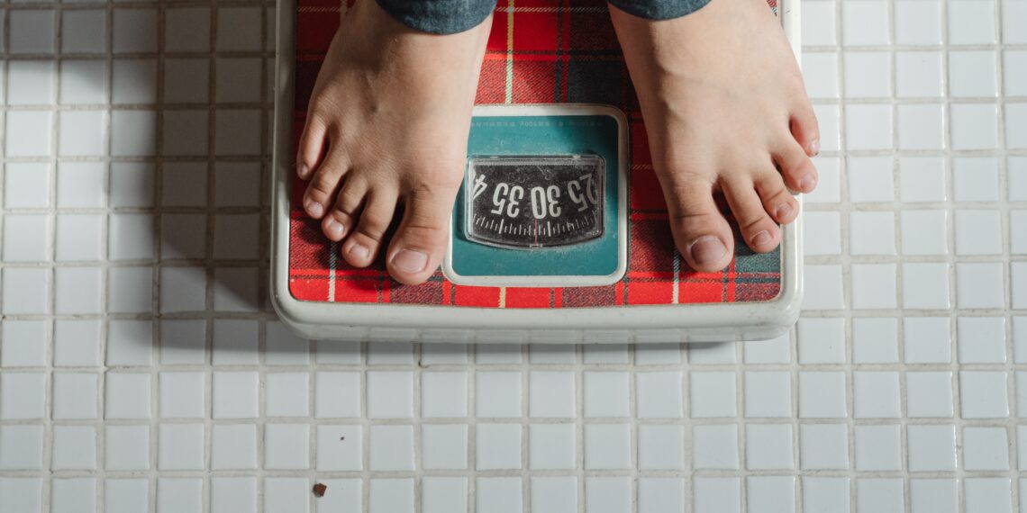 A person weighing themselves on a red and green retro looking weighing scale
