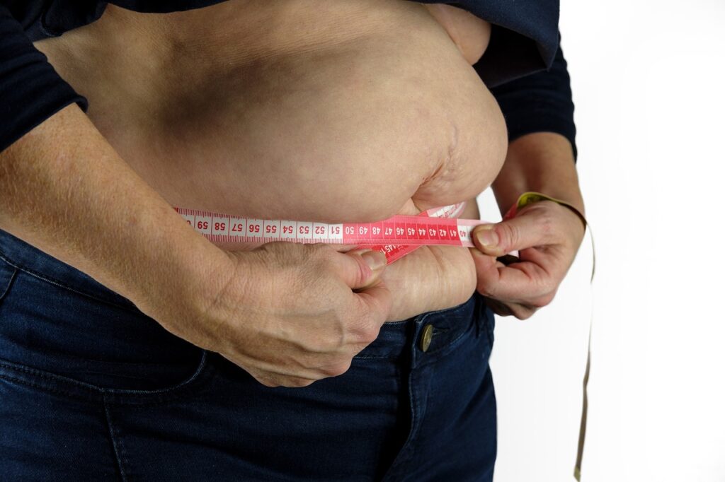 An overweight midsection is being measured with a measuring tape