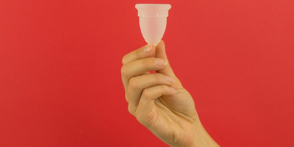 A hand holding a small plastic cup in front of a red background