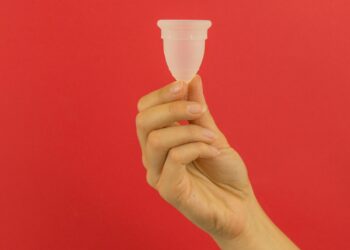 A hand holding a small plastic cup in front of a red background