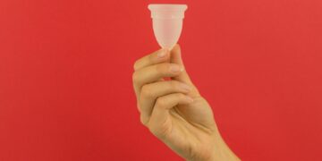 A hand holding a small plastic cup in front of a red background