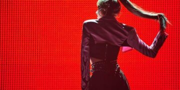 lisa manoban dressed in performance outfit posing and standing against a red background