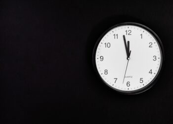 White round clock showing 90 seconds to midnight on black wall.
