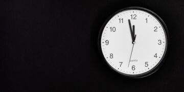 White round clock showing 90 seconds to midnight on black wall.