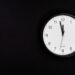 White round clock showing 90 seconds to midnight on black wall.