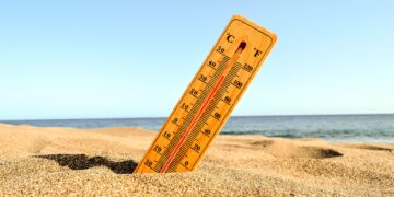 closeup-shot-of-yellow-wooden-thermometer-partly-buried-in-sand-with-blue-beach-backdrop