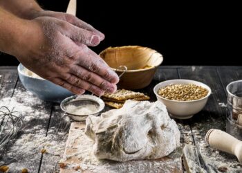 hands-sprinkling-flour-on-a-dough-placed-on-a-wooden-board
