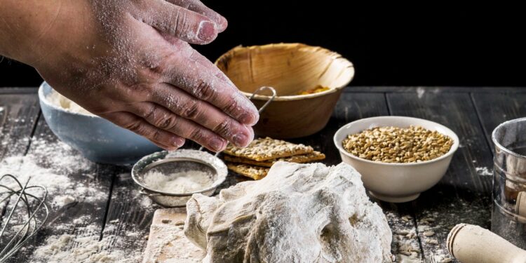hands-sprinkling-flour-on-a-dough-placed-on-a-wooden-board