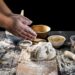 hands-sprinkling-flour-on-a-dough-placed-on-a-wooden-board